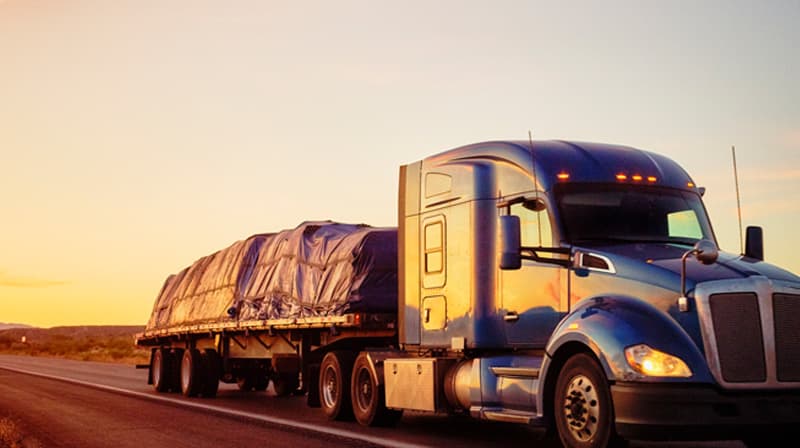 A flat deck tractor-trailer hauling secured cargo on a wet highway